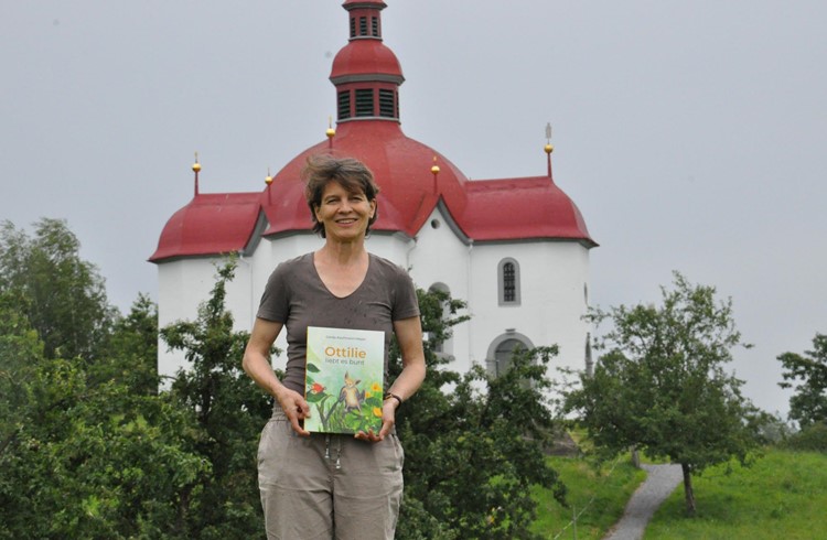 Gerda Kaufmann-Meyer mit dem neu gedruckten Bilderbuch vor der Kapelle St. Ottilien. Die Kapelle mit ihrer Fledermauskolonie sorgte für den zündenden Funken. Foto zVg