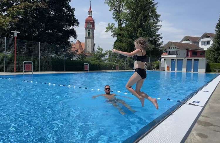 Soley Habermacher geniesst mit einem Sprung ins Wasser die Erfrischung, beobachtet von Vater Etienne. Foto Stefan Schmid